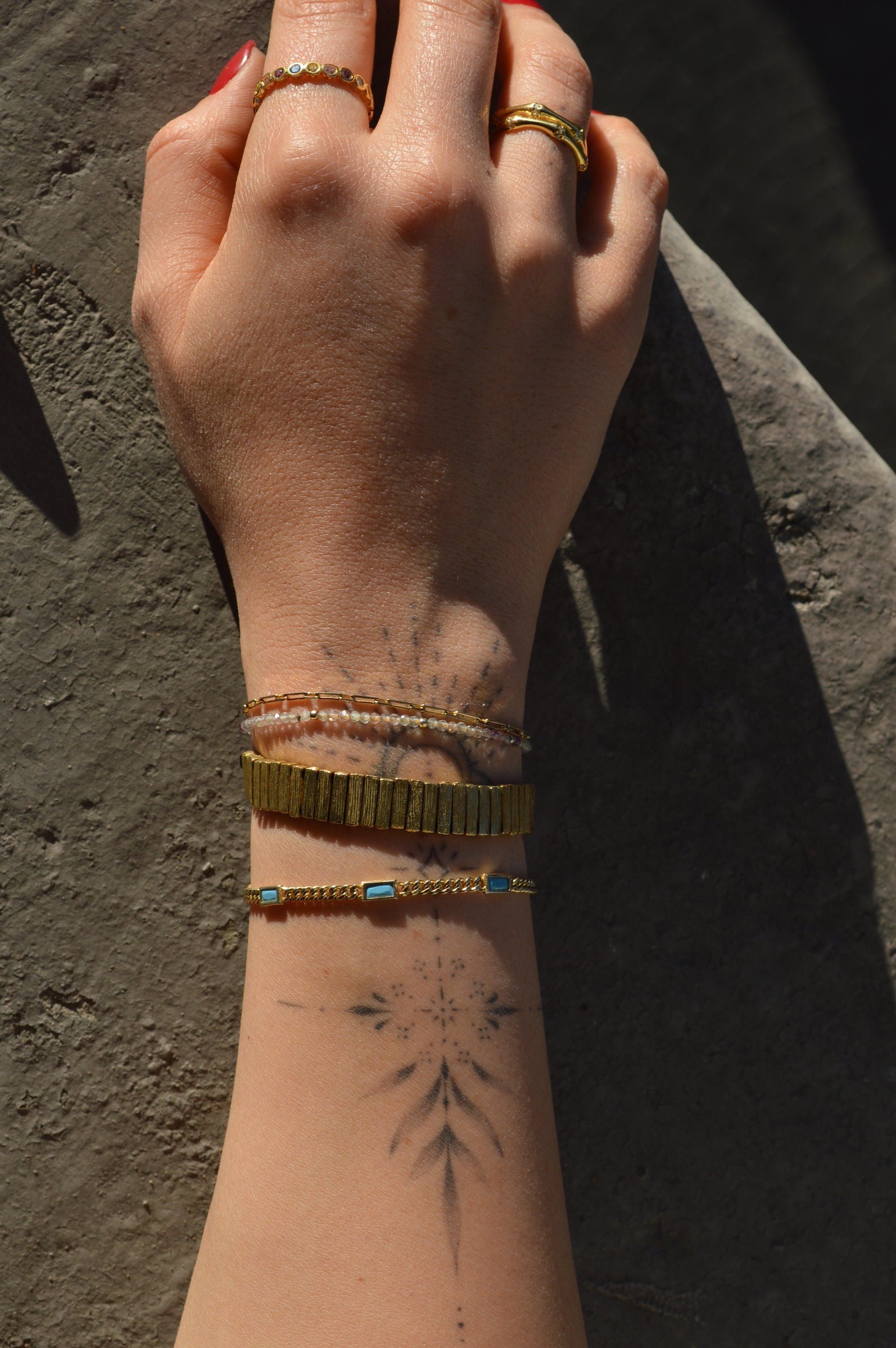 Close-up of a person's arm with tattoos and jewelry on a dark surface